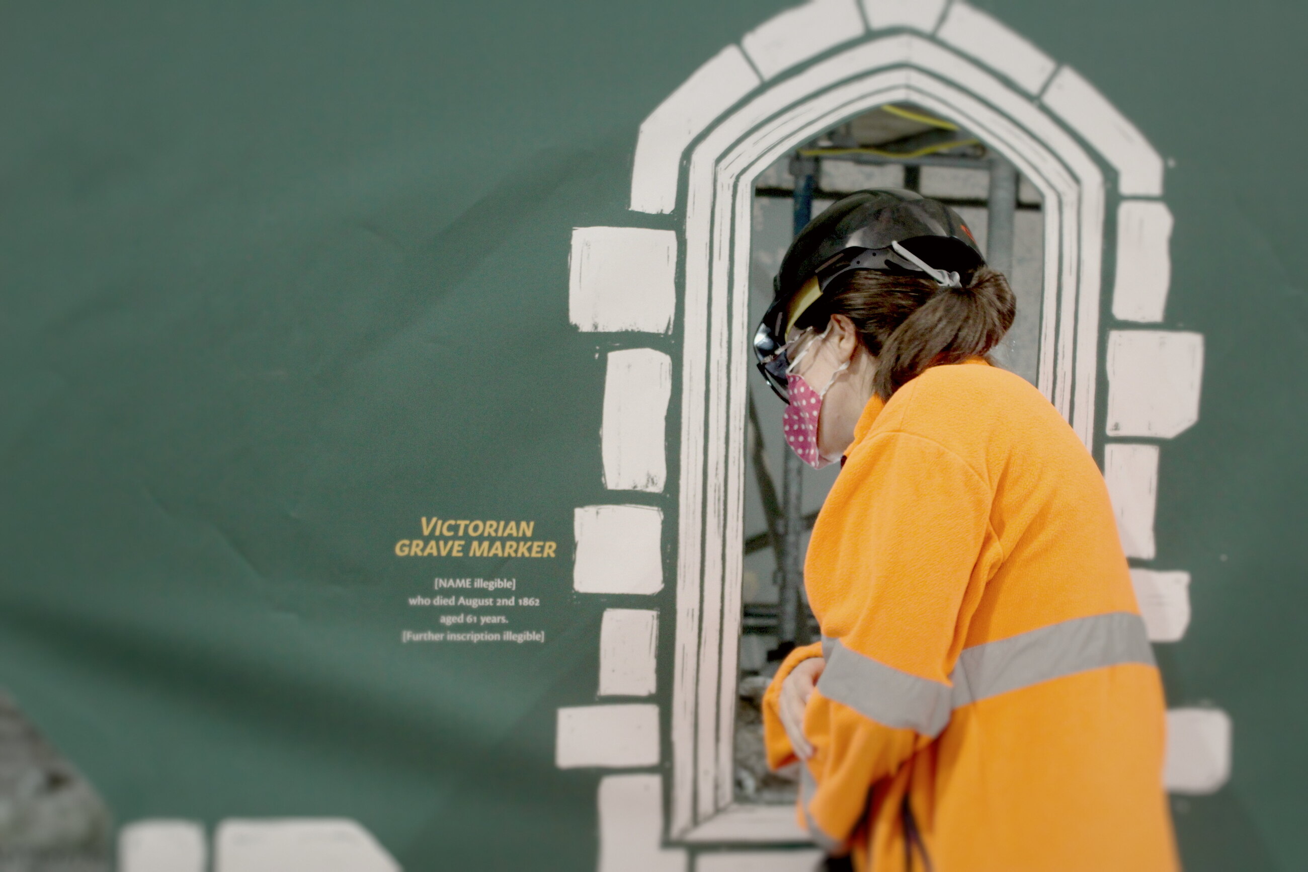 A visitor in hi-vis looking through a cut-out church window.