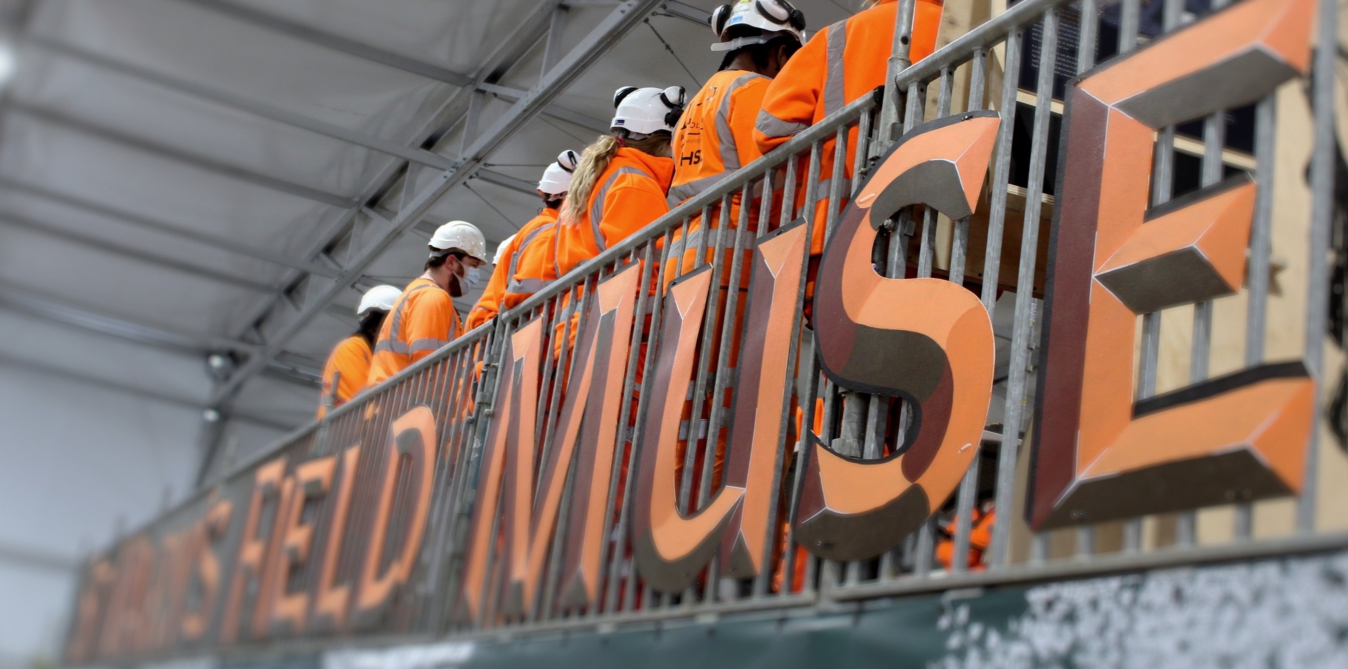 Visitors in hard hats behind the Field Museum lettering.